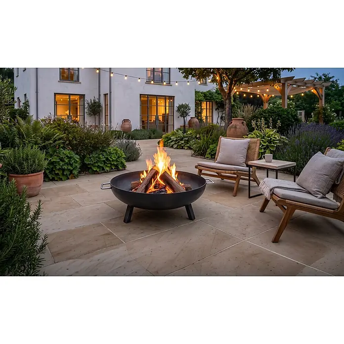 Brasero Lume con patas - Diámetro: 60 cm, Acero - Brasero de metal negro con leños ardiendo en un patio exterior, rodeado de sillas y plantas de jardín.