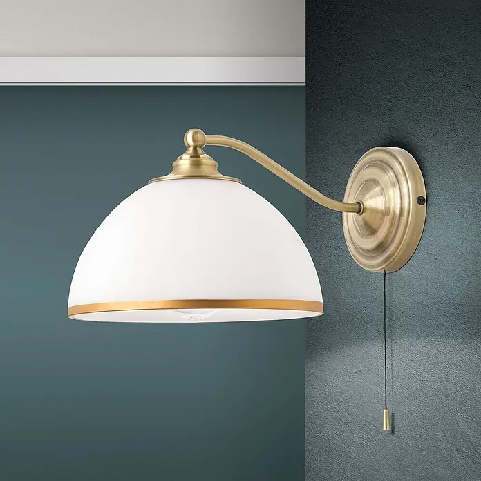 Orion Leuchten Wandleuchte - 40 W, L x B x H: 32 x 22 x 16 cm, E27 - Messing-Wandleuchte mit weißem Kuppelschirm und Zugschalter an dunkelblauer Wand.