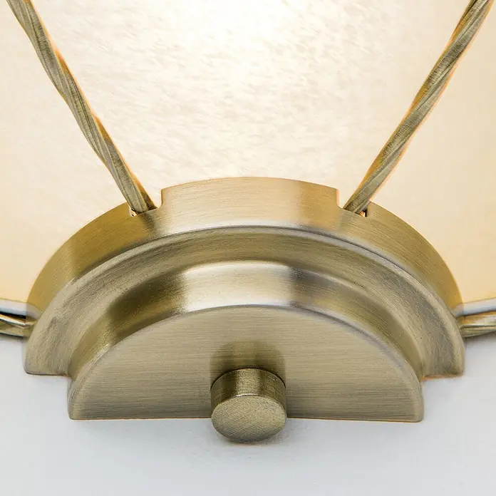 Orion Leuchten Wandleuchte - 60 W, L x B x H: 16 x 31 x 13 cm, E27 - Nahaufnahme einer antikisierten Messing-Leuchtenbasis mit kleinem Knopf und gedrehten Metallarmen, die einen durchscheinenden, beleuchteten, strukturierten Schirm halten.