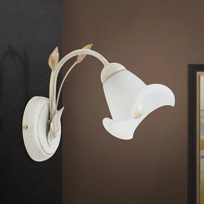 Orion Leuchten Wandleuchte - 40 W, L x B x H: 26 x 14 x 22,5 cm, E14 - Wandleuchte aus antikweißem Metall mit Blattdetails und weißem mattiertem Glas in Form einer Calla-Blume, an einer dunklen Wand montiert.