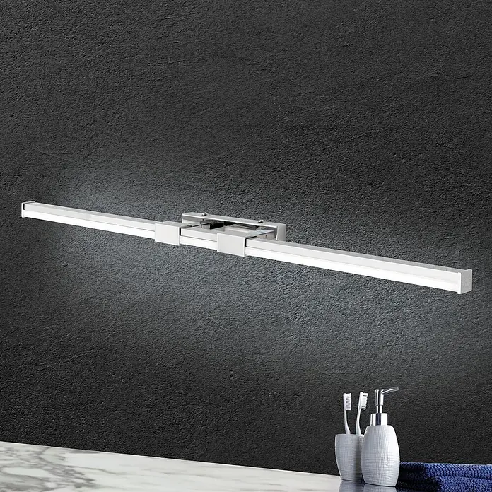 Orion Leuchten Wandleuchte - 17 W, L x B x H: 8 x 75 x 5 cm - Lineare LED-Spiegelleuchte in Silberoptik an dunkler Wand, beleuchtet eine Waschtischplatte mit Badaccessoires.