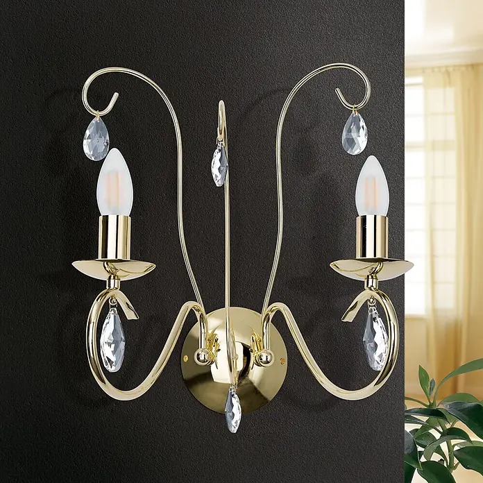 Orion Leuchten Wandleuchte - 40 W, L x B x H: 26 x 37 x 45 cm, E14 - Elegante goldfarbene Wandleuchte mit zwei Kerzenlichtern und klaren Kristalltropfen, an einer dunklen Wand in einem Raum montiert.