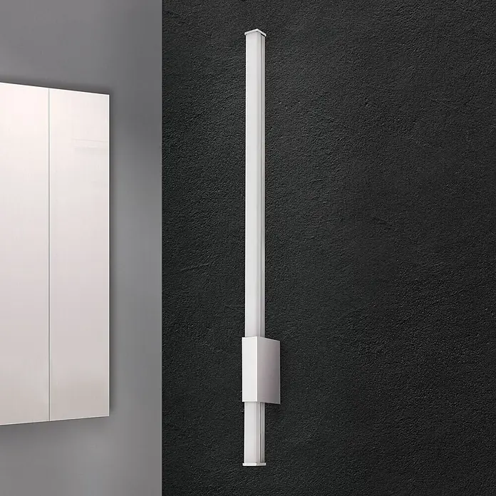 Orion Leuchten Wandleuchte - 13 W, L x B x H: 6,8 x 60,5 x 2,5 cm - Silberfarbene, lineare LED-Wandleuchte, vertikal an dunkler Wand neben weißem Schrank montiert.
