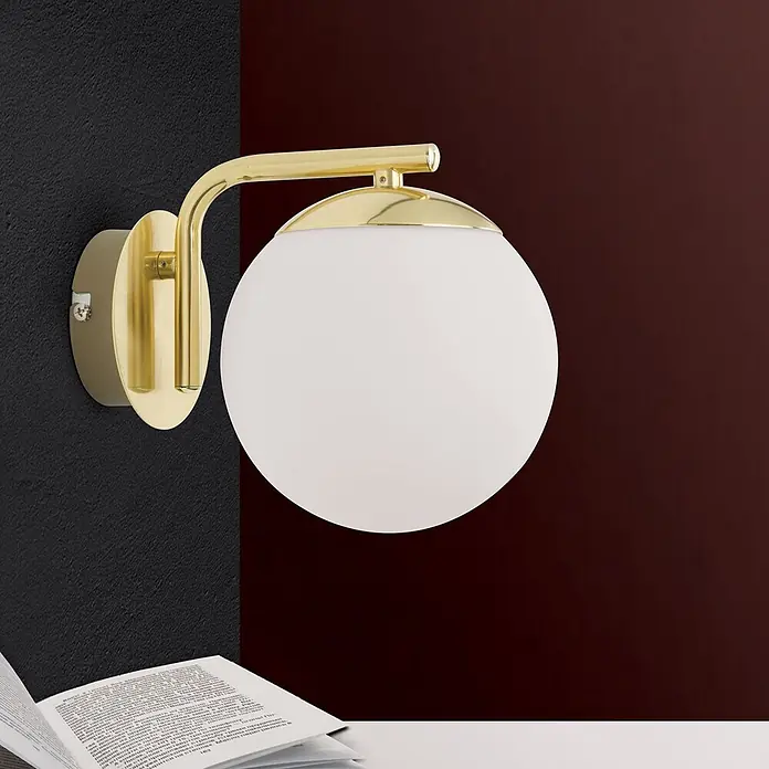 Orion Leuchten Wandleuchte - 40 W, L x B x H: 21 x 15 x 17 cm, E14 - Goldene Wandleuchte mit kugelförmigem weißem Glasschirm an der Wand über einem offenen Buch.