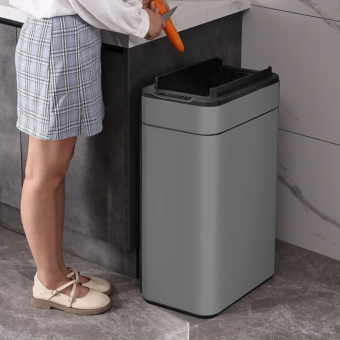 SVITA Sensormülleimer SE60L - 60 l, Stahl, Grau - Person schält Karotten in einen grauen, rechteckigen Smart-Mülleimer mit offenem Deckel in einer modernen Küche.