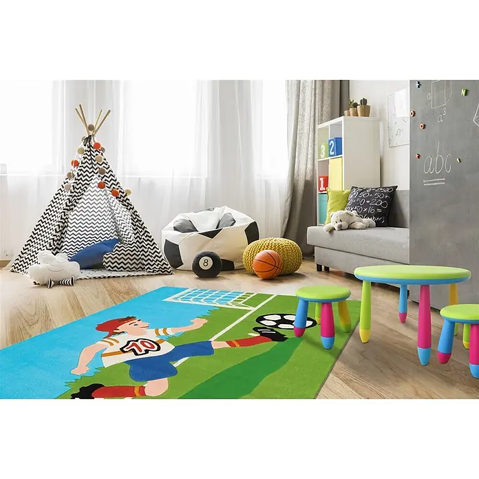 Kayoom Kinderteppich Joy 4090 - Multi, 160 x 110 cm, 100 % Modacryl - Bunter Fußballteppich auf Holzboden im Kinderzimmer, mit einem Jungen, der einen Ball auf grünem Feld tritt.