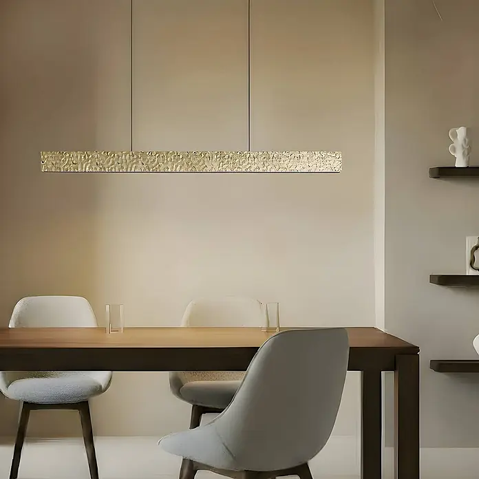 Lucande Pendelleuchte Nivara - messing / gold, gold, Schwarz - Texturierte goldene lineare Pendelleuchte beleuchtet einen Esstisch in einem modernen Raum.