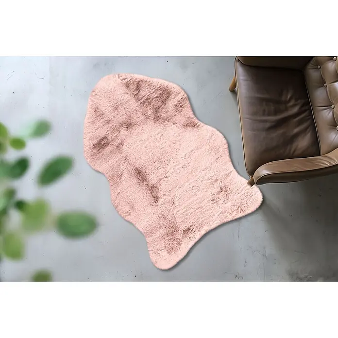 Kayoom Kunstfell Boundless 226 - Puderrosa, 90 x 60 cm, 90 % Polyester, 10 % Baumwolle - Rosa Kunstfell-Teppich auf grauem Boden neben einem braunen Sessel.