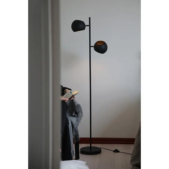 Markslöjd Stehleuchte Edgar - 40 W, Höhe: 145 cm, Schwarz, E14 - Schwarze Stehlampe mit zwei kugelförmigen Schirmen, neben einer lesenden Person für Ambiente- und Arbeitsbeleuchtung.