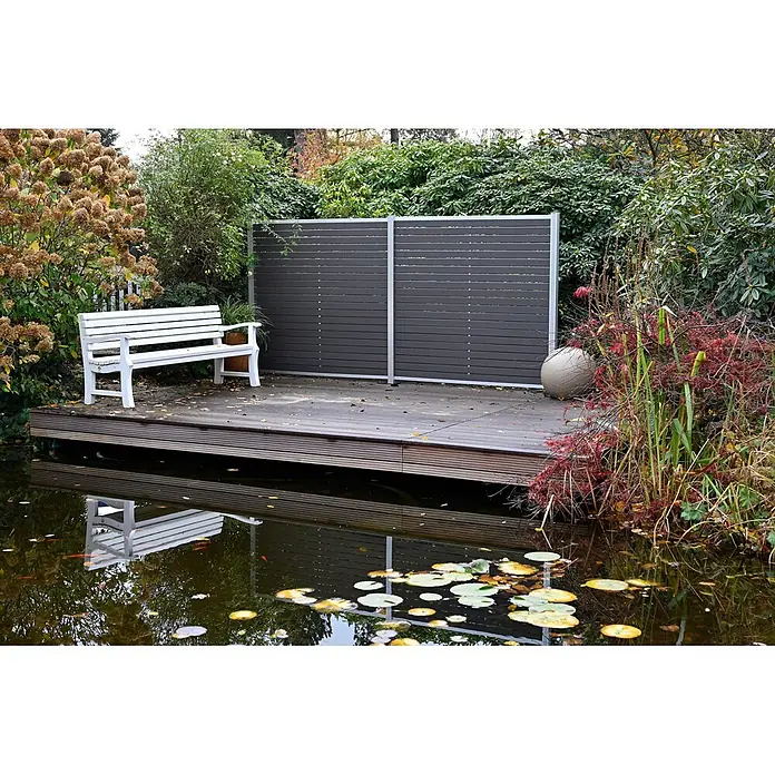 GartenLand Steckzaun-Element WPC Zaun Stockholm Musterstück - B x H: 20 x 7,5 cm, Anthrazit, Verbundwerkstoff - Weiße Holzbank auf Holzterrasse am Teich, mit dunkelgrauem Sichtschutz und üppigen Gartenpflanzen.