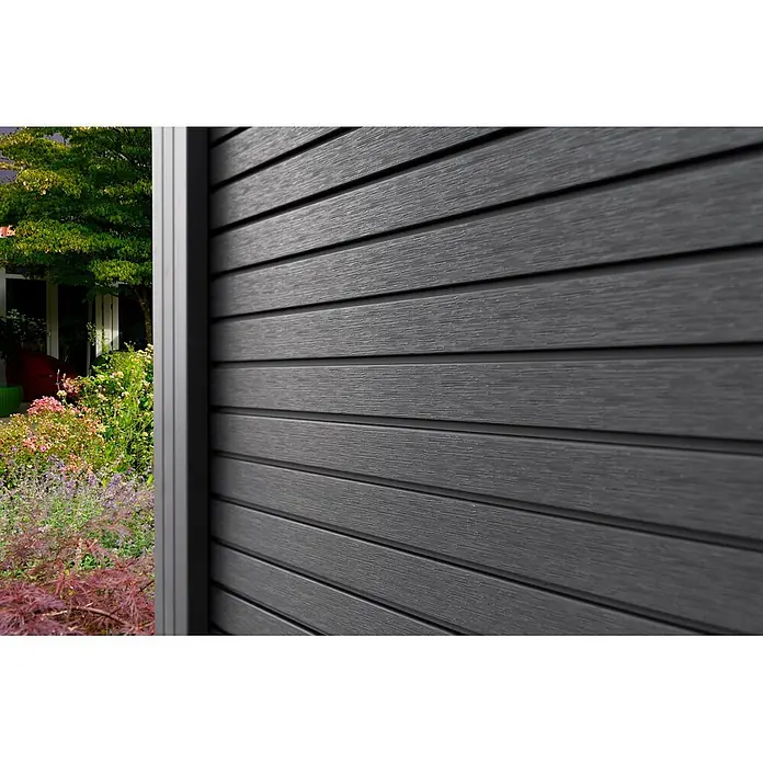 GartenLand Steckzaun-Element WPC Zaun Shadowline Ohne Pfosten - B x H: 180 x 180 cm, Deep Black, Verbundwerkstoff - Dunkelgraue horizontal angebrachte Verbundverkleidung, die teilweise einen lebhaften Garten und ein Haus verdeckt.