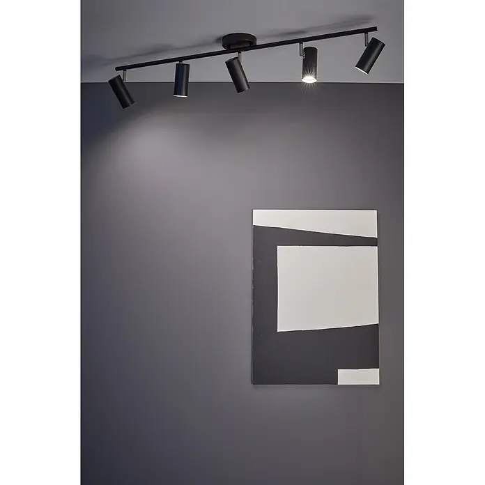 Markslöjd Deckenstrahler Barcelona - 12 W, L x B x H: 20 x 109 x 23 cm, Schwarz, GU10 - Schwarze Deckenleuchte mit Strahlern, die eine graue Wand und ein abstraktes schwarz-weißes Gemälde beleuchten.