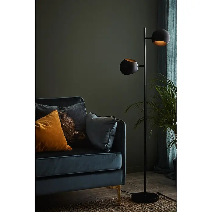Markslöjd Stehleuchte Edgar - 40 W, Höhe: 145 cm, Schwarz, E14 - Dunkelblaues Samtsofa mit goldenen Beinen, orangefarbenen und Paillettenkissen sowie schwarze Doppel-Stehleuchte auf gewebtem Teppich.