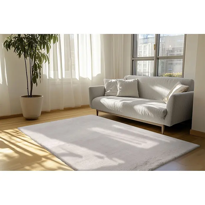 Kayoom Fellteppich Luxe 525 - Polargrau, 230 x 160 cm, 90 % Polyester, 10 % Wolle - Hellgrauer, texturierter Teppich auf Holzfußboden in hellem Wohnzimmer, teilweise unter einem grauen Sofa platziert.