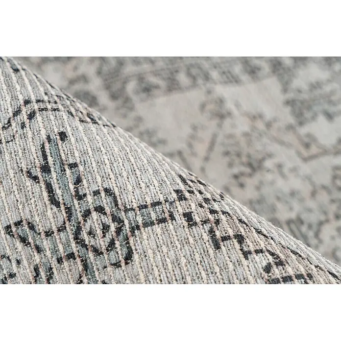 Kayoom Flachgewebeteppich Perry 325 - Grün/Taupe, 170 x 120 cm, 75 % Baumwolle, 25 % Polyester - Nahaufnahme eines gerollten, grau-blau gemusterten Teppichs, der seine gewebte Textur zeigt.