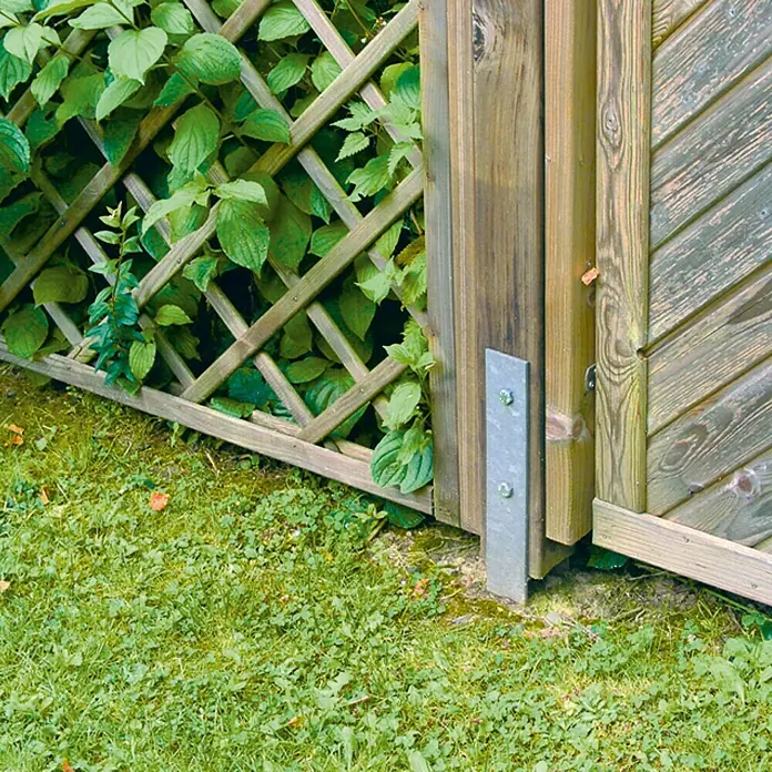 Stabilit H-Pfostenanker Typ 365 - 121 x 60 x 600 mm - Nahaufnahme eines Gartenzauns mit einem silbernen Metallbeschlag, der die Holzkonstruktion verstärkt und für Stabilität sorgt.
