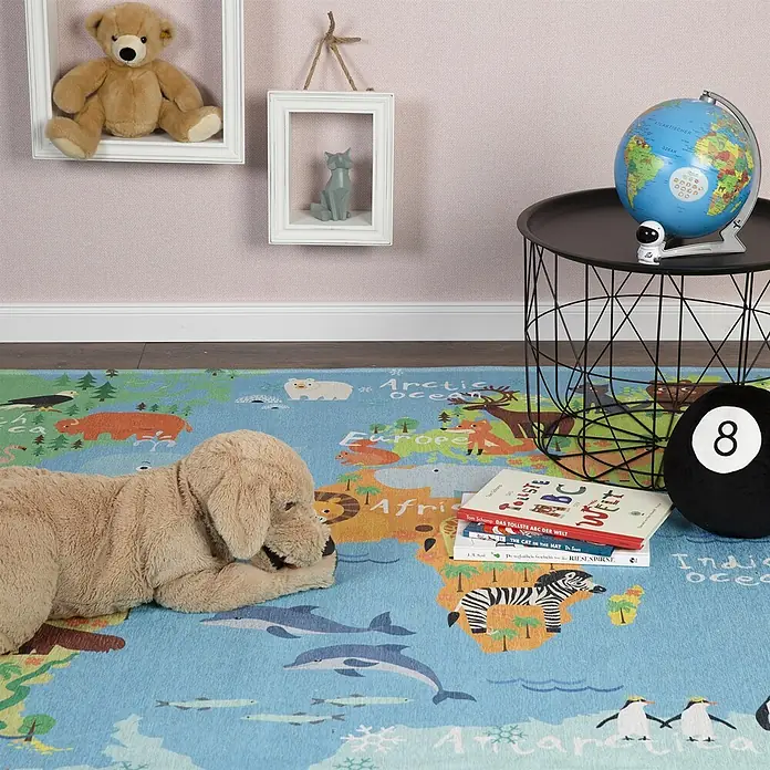 Kayoom Kinderteppich Sympathy Kids 243 World Map - Multi, 230 x 160 cm, 100 % Polyester - Ein blauer Weltkarten-Teppich mit Tieren und Kontinenten auf dem Boden eines Kinderzimmers mit Plüschhund, Büchern und Globus.
