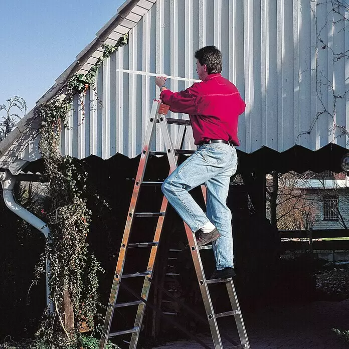 Krause Escalera multiusos - Altura de trabajo: 5,25 m, Número de peldaños: 18 ud., Carga soportada: 150 kg, Aluminio - Hombre de pie sobre una escalera de tijera de aluminio plateado junto a una fachada.