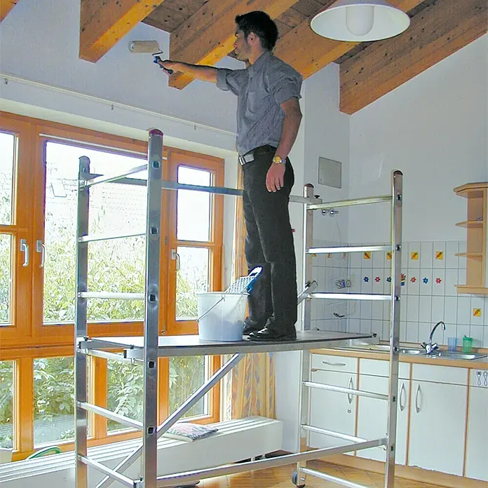 Krause Corda Kleingerüst - Arbeitshöhe: 3 m - Mann auf einem Layher Fahrgerüst beim Streichen der Decke. Das Gerüst bietet sicheren Stand und Flexibilität bei Renovierungsarbeiten.