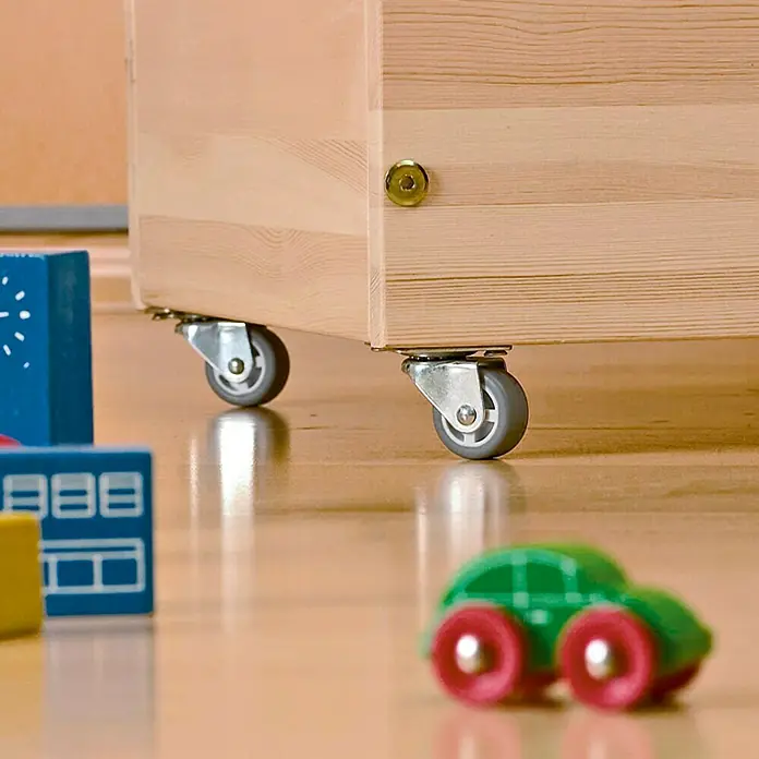 Stabilit Rueda giratoria para muebles - Diámetro: 45 mm, Capacidad de carga: 40 kg, Gris, Plástico - Primer plano de un mueble de madera con ruedas grises sobre un suelo de madera lisa, rodeado de bloques de juguete de colores y un coche pequeño.