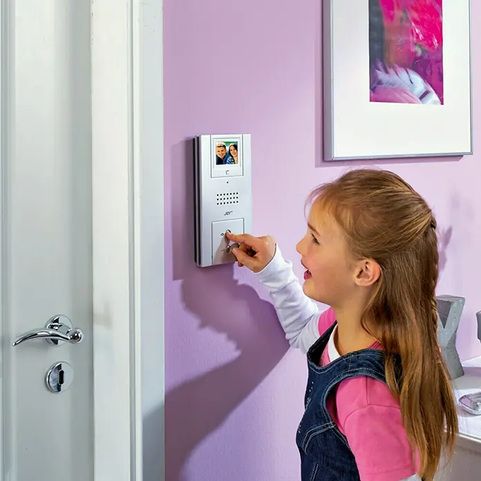 Farb-Video-Türsprechanlage Quattroline - 1-Familienhaus, 3,4″ - Ein Mädchen klingelt an einer JAY-Türsprechanlage mit integriertem Display an einer lila Wand neben einer weißen Tür.