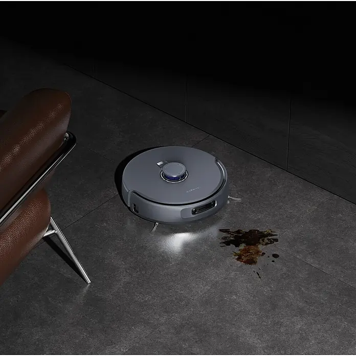 Narwal Saugwischroboter Freo Z ultra - Saugkraft: 12.000 Pa - Ein grauer Roboterstaubsauger steht auf dunklen Fliesen neben einem dunklen Fleck, was seine Reinigungsfunktion hervorhebt.