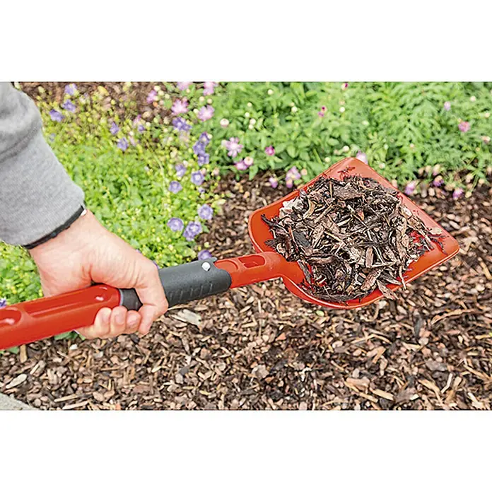Gardol Klappschaufel - Kunststoff - Nahaufnahme einer roten Gartenschaufel gefüllt mit Mulch vor einem Blumenbeet.