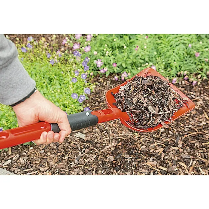 Gardol Klappschaufel - Kunststoff - Nahaufnahme einer roten Gartenschaufel gefüllt mit Mulch vor einem Blumenbeet.