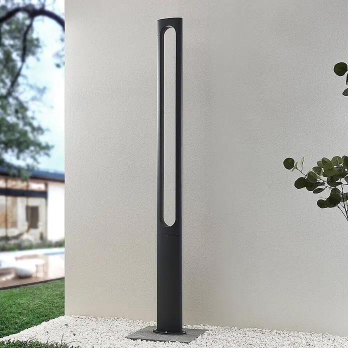 Lucande LED Gartenlaterne für draußen in dunkelgrau, Mastleuchte -  - Hohe dunkelgraue Außenpollerleuchte mit länglicher Öffnung oben, auf weißen Kieseln zur Wegbeleuchtung installiert.
