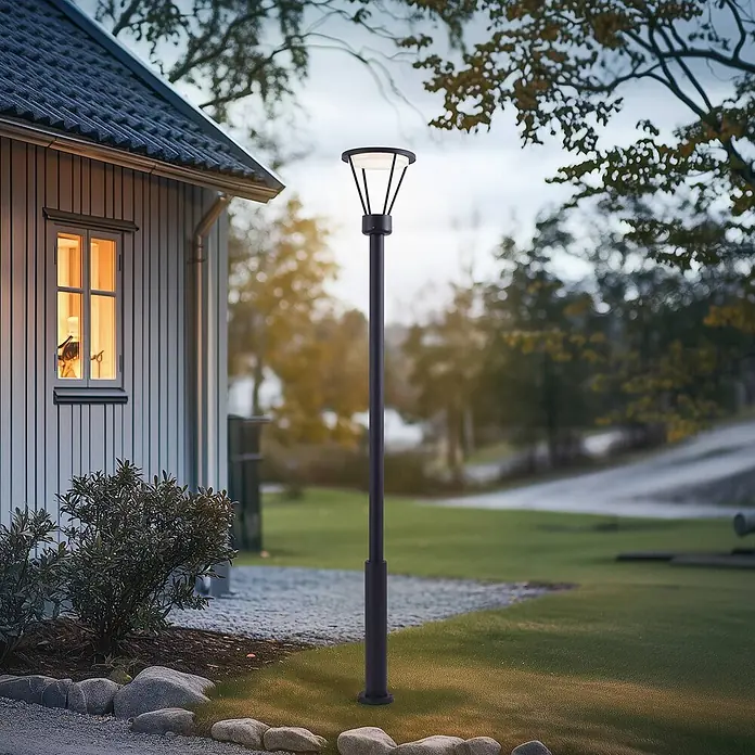 Lucande LED Gartenlaterne für draußen in schwarz matt, Mastleuchte -  - Dunkle Metall-Gartenleuchte erhellt einen Weg im Garten bei Dämmerung, neben einem Haus.
