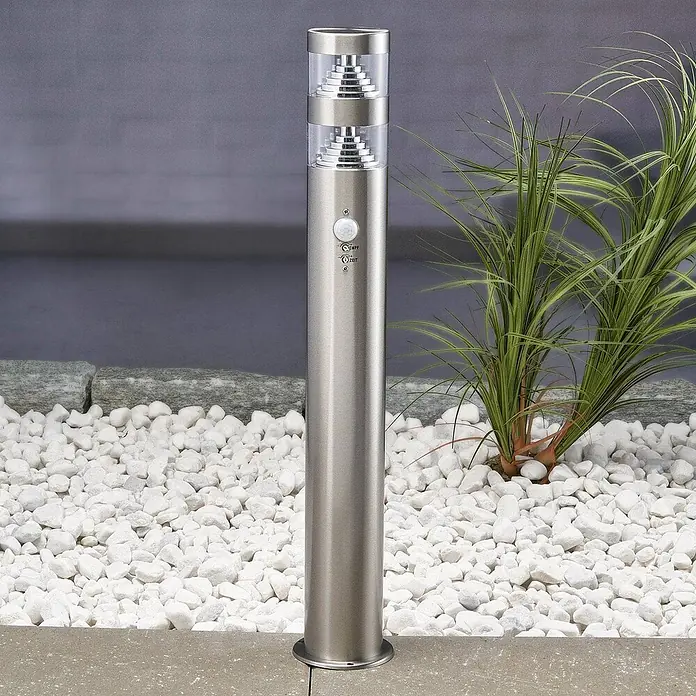 Lindby Edelstahl LED Wegeleuchte / Pollerleuchte 60 cm mit Bewegungsmelder -  - Edelstahl-Pollerleuchte für außen mit Bewegungsmelder, umgeben von weißen Kieselsteinen und grünen Pflanzen.