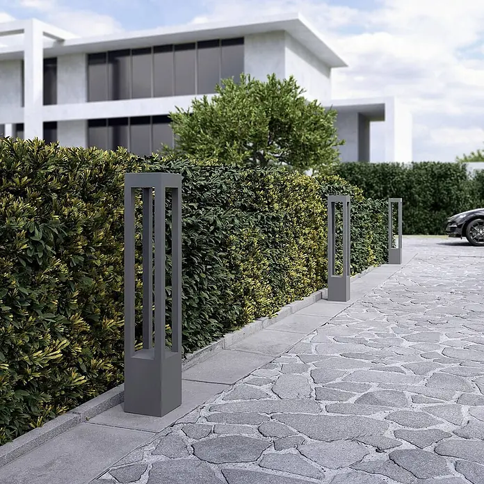Arcchio LED Wegeleuchte in dunkelgrau, Gartenlampe -  - Dunkelgraue, rechteckige Pollerleuchten mit offenem Rahmen beleuchten eine Steineinfahrt entlang einer grünen Hecke.