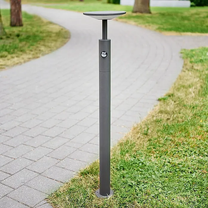 Lucande LED Wegeleuchte mit Bewegungsmelder Gartenleuchten mit Strom 100cm -  - Anthrazitfarbene zylindrische Pollerleuchte mit flacher Oberseite und Seitensensor, an einem gepflasterten Weg installiert.