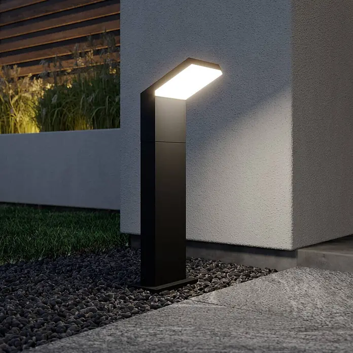 Arcchio LED Wegeleuchte in dunkelgrau, weiß, Gartenlampe -  - Schwarze, moderne Pollerleuchte beleuchtet einen Kiesweg und eine Wand in einem zeitgenössischen Garten.