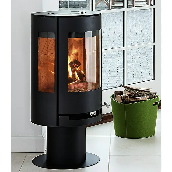 Aduro Kaminofen 9-3 - 8 kW, Raumheizvermögen: 350 m³, Material Verkleidung: Stahl, Schwarz - Ein eleganter, schwarzer Kaminofen mit loderndem Feuer und einem grünen Holzkorb neben einem Fenster. Wärmende Atmosphäre für Ihr Zuhause.