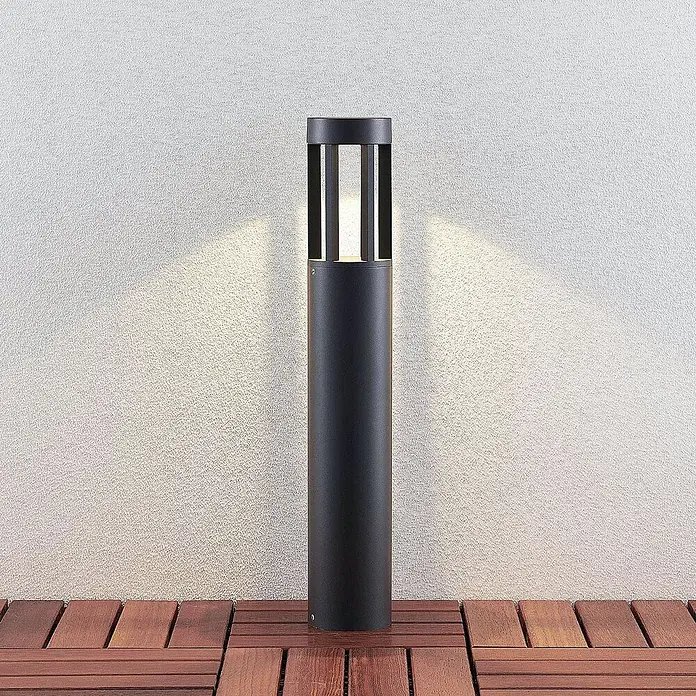 Lucande LED Wegeleuchte, Pollerleuchte Dunkelgrau, Außenleuchte 65 cm -  - Schwarze zylindrische Außenleuchte auf Holzterrasse, die Licht nach oben und an eine strukturierte Wand abgibt.