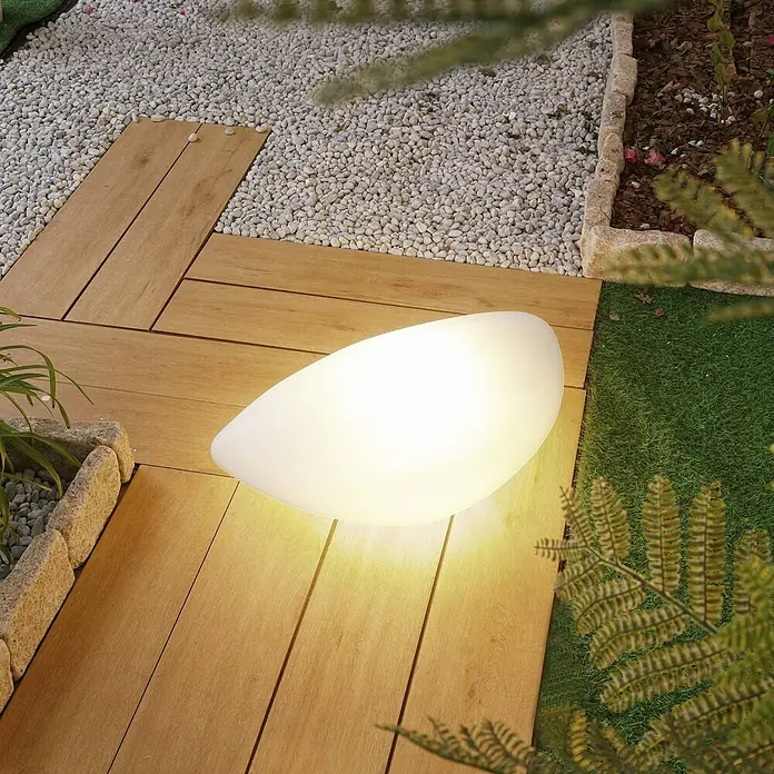 Lindby LED Dekorationsleuchte in weiß, schwarz, -  - Eine beleuchtete weiße, ovale Außenleuchte auf Holzterrasse, die warmes Licht abstrahlt.