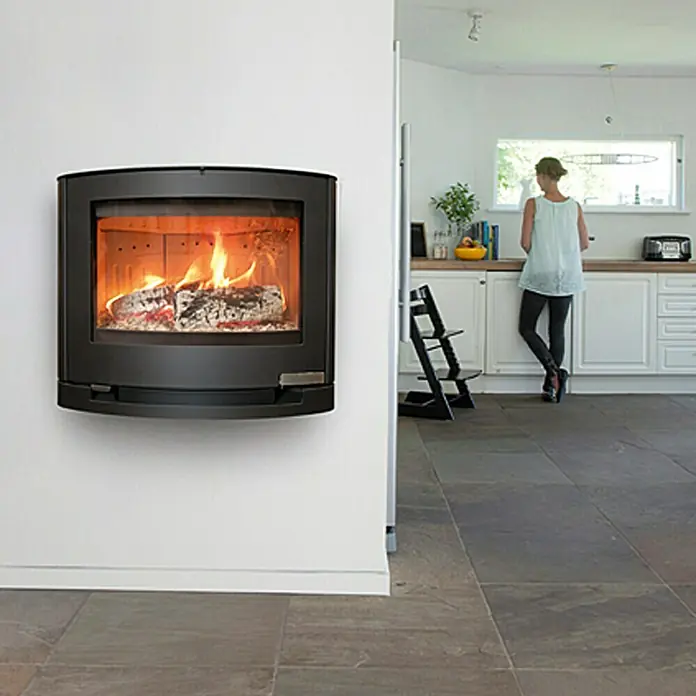 Aduro Kaminofen 15-3 - 6,5 kW, Raumheizvermögen: 334 m³, Material Verkleidung: Stahl, Schwarz - Wandmontierter Kaminofen mit brennendem Holz in einem modernen Haus, der Wärme und Stil vereint. Ideal für gemütliche Abende.