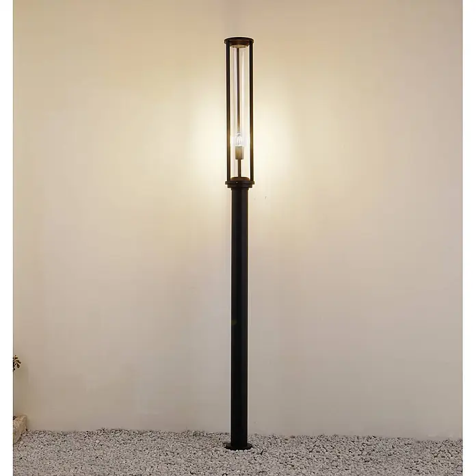 Lucande Außenlaterne Alivaro -  - Hohe schwarze Außenleuchte mit klarem Zylinder, steht auf weißen Kieseln.