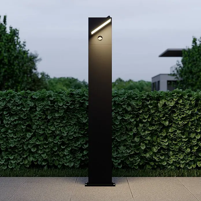 Lucande Außenlaterne Silvan -  - Schwarze Gartenleuchte mit schrägem LED-Licht und Sensor, beleuchtet einen Weg neben einer Hecke.