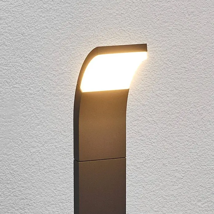 Lucande Außenlaterne Timm -  - Moderne anthrazitfarbene Außenwandleuchte mit gebogener Oberseite, strahlt warmweißes Licht auf eine Strukturwand.