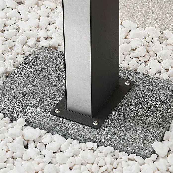 Lucande Außenlaterne Aegisa -  - Sockel eines schwarz-silbernen Pfostens auf einer Granitplatte, mit Schrauben befestigt und von weißen Zierkieseln umgeben.