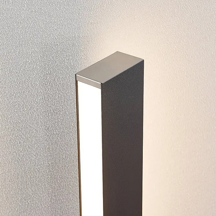 Lucande Außenlaterne Aegisa -  - Dunkelgraue LED-Außenwandleuchte mit gebürsteter Stahlplatte, an einer Wand montiert, strahlt warmes Licht aus.