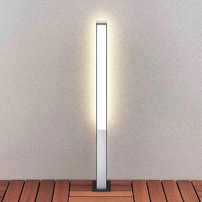 Lucande Außenlaterne Aegisa -  - Schlanke, lineare, silbergraue Außenleuchte mit weißem LED-Bereich, auf Holzdielen montiert, beleuchtet eine strukturierte Wand.