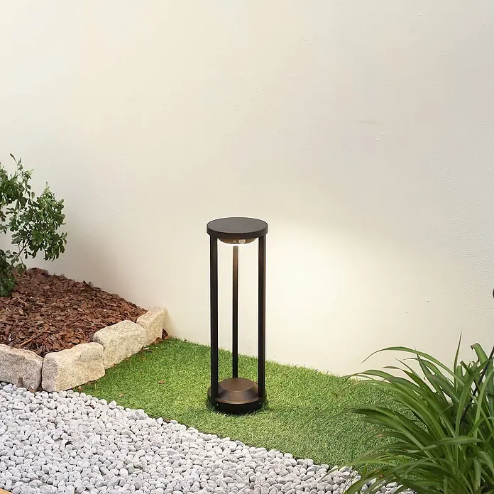 Lucande Außenlaterne Nilea -  - Dunkle Metall-Gartenleuchte, die eine Kunstrasenfläche in einem Garten beleuchtet.