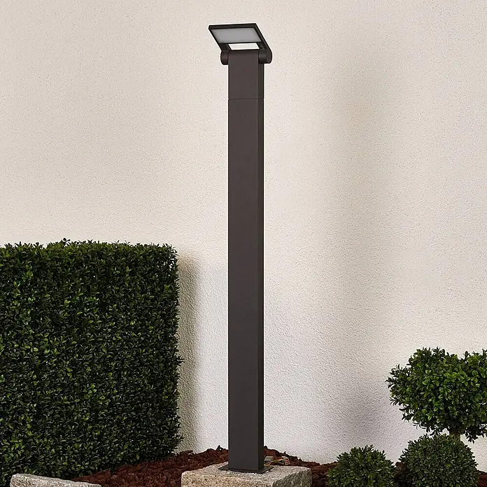 Lucande LED Wegeleuchte in graphit, weiß, Gartenlampe -  - Dunkelgraue quadratische Außenpollerleuchte mit verstellbarem LED-Kopf, in einer Gartenumgebung neben Hecken installiert.