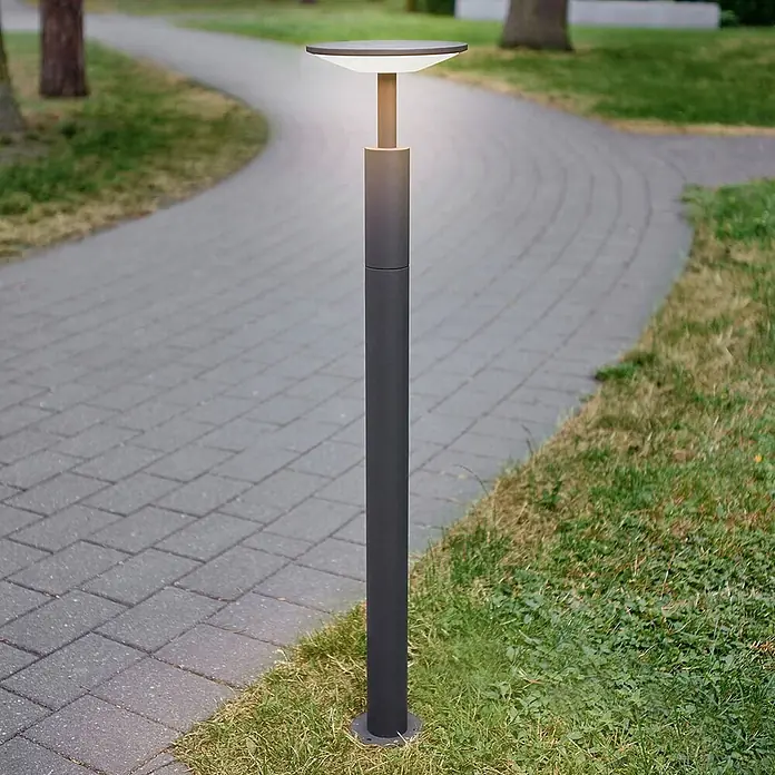 Lucande LED Wegeleuchte anthrazit Gartenlampe 100cm Pollerleuchte Aluminium -  - Dunkelgraue Wegeleuchte mit warmem Licht, neben einem gepflasterten Weg in einer grünen Parklandschaft.