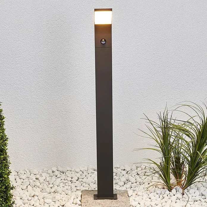 Lucande Außenlaterne Timm -  - Anthrazitfarbene Wegeleuchte mit Bewegungssensor und hellem Licht, beleuchtet einen modernen Gartenweg mit Kieselsteinen.