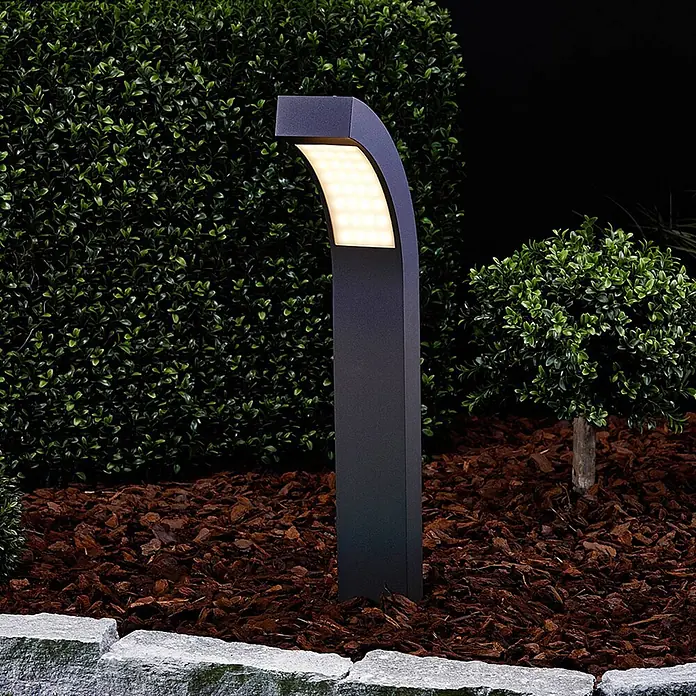 Lucande LED Sockelleuchte, Wegeleuchte außen, Höhe: 60 cm, inkl. 4,2W LED -  - Anthrazitfarbene Außenwegleuchte mit gebogenem Oberteil und integriertem LED-Panel, beleuchtet ein Gartenbeet mit Mulch und Pflanzen.