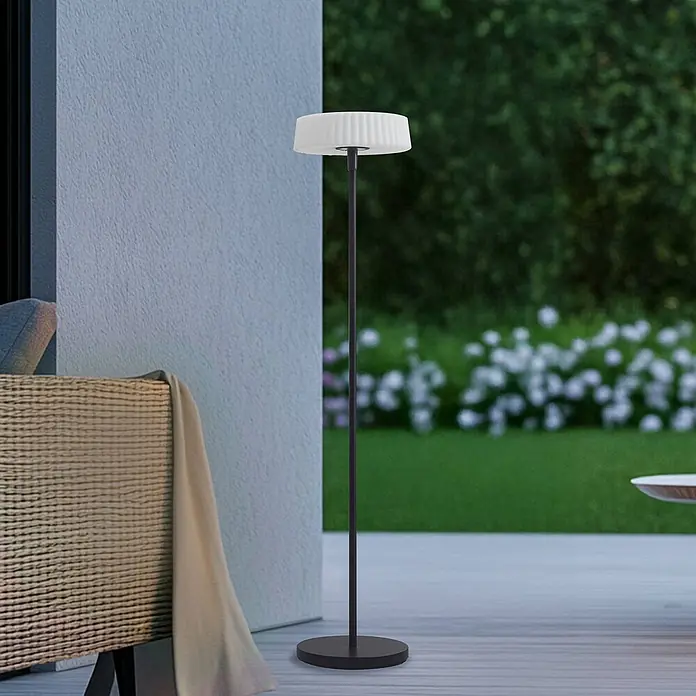 Lindby LED Solar Stehlampe Outdoor in schwarz, weiß, dimmbar Stehleuchte -  - Große Outdoor-Stehleuchte mit dunklem Metallfuß und weißem, plissiertem zylindrischem Schirm auf einer Terrasse.